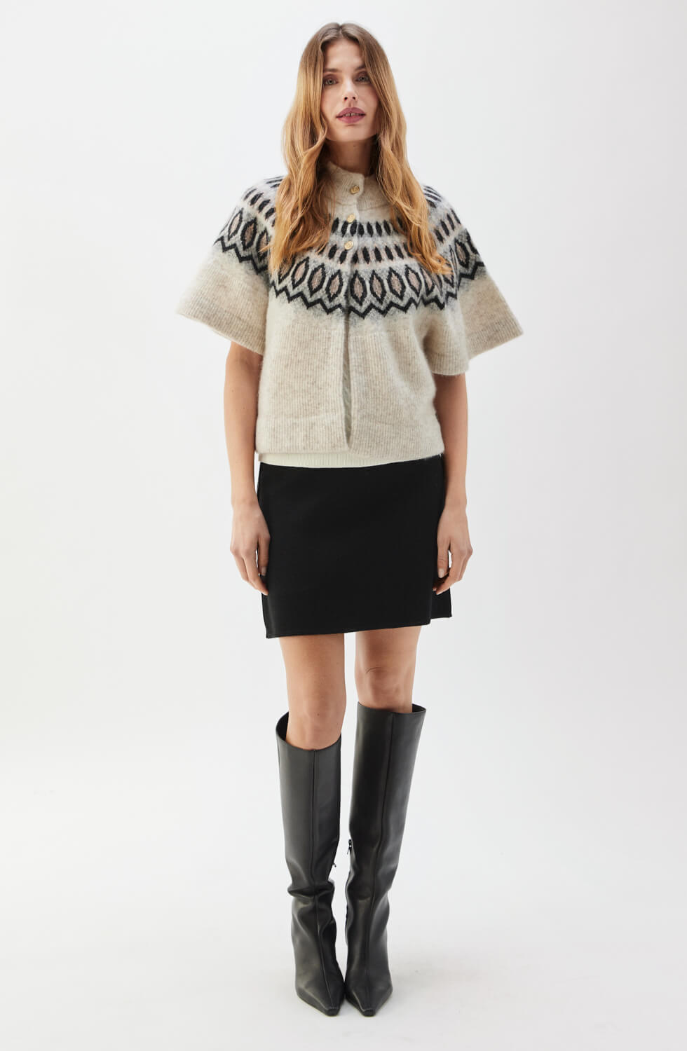 Woman wearing a patterned sweater and black skirt with knee-high boots on a white background